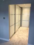 Showing the wardrobes doors on the left side of the corridor, which are soft white glass with polished silver frames