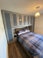 Fitted Hinged wardrobes with over bed cupboards in conrete wood with blue glass (angled view)