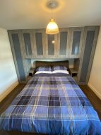 Fitted Hinged wardrobes with over bed cupboards in conrete wood with blue glass (straight on view)